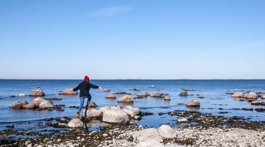 Nainen loikkaa rantakiven päälle Örössä Saaristomerellä